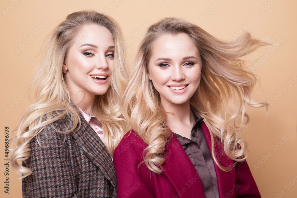 fashion portrait of two girls, best friends posing indoor on beige background wearing winter stylish coat. fashion portrait of two girls, best friends posing indoor on beige background wearing winter stylish coat.