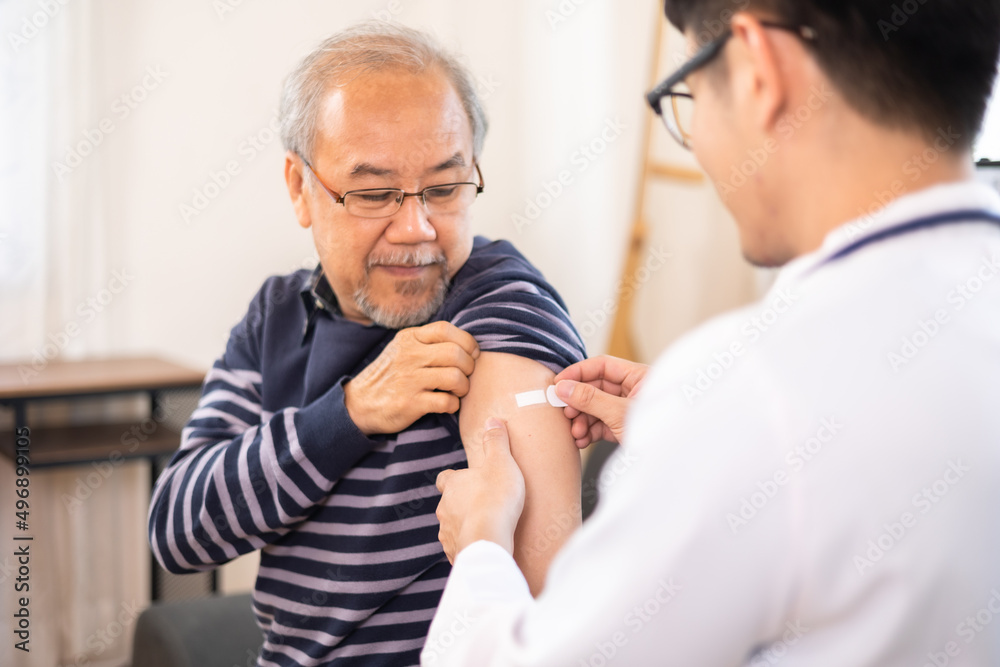 Safe vaccination for old people. Elder man in medical  getting flu or Covid-19 vaccine sitting on sofa at home. Asian Doctor or nurse giving flu or Covid-19 shot to senior. - obrazy, fototapety, plakaty 