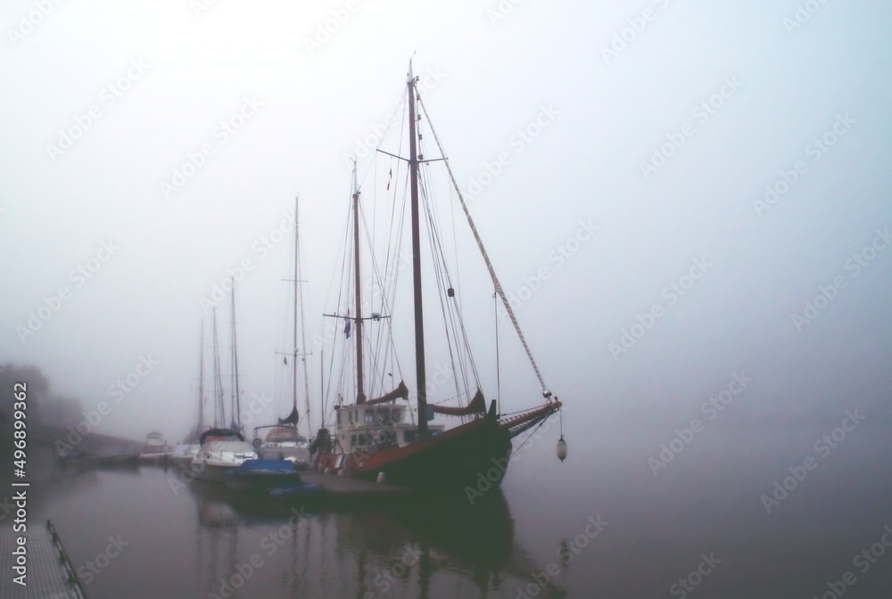Veleros atracados en un muelle flotante y rodeados de niebla. Puerto fluvial de Sanlúcar de Guadiana una mañana sin viento y fría de noviembre. Sanlúcar de Guadiana, Huelva, España.