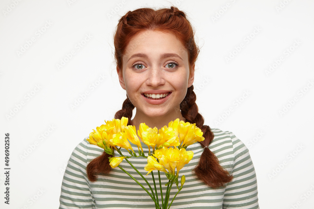 Indoor portrait of young ginger female posing over white background holding bouquet of flowers and smile broadly Indoor portrait of young ginger female posing over white background holding bouquet of flowers and smile broadly