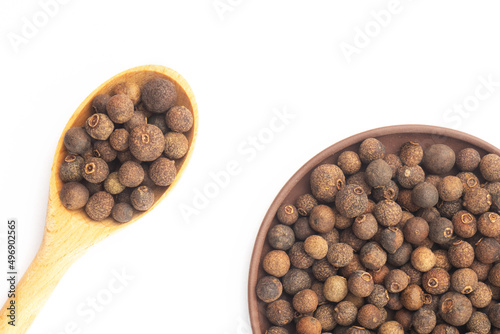 Spice Allspice in wooden spoon diagonally and clay plate on white background. Flat lay. Healthy eating concept