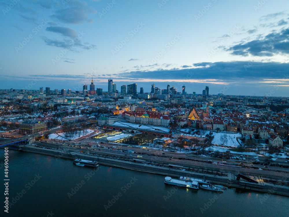 Fototapeta premium Widok na zamek królewki i stare miasto w Warszawie z drona, w tle wieżowce, zaśnieżone dachy, zachód słońca