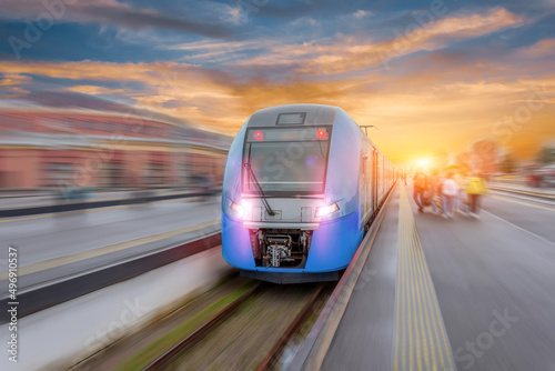 Railway station with modern high speed red commuter train with motion blur effect at colorful beautiful sunset.