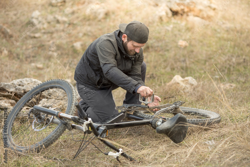 Obraz premium a young male cyclist is sitting on the grass and repairing a mountain bike