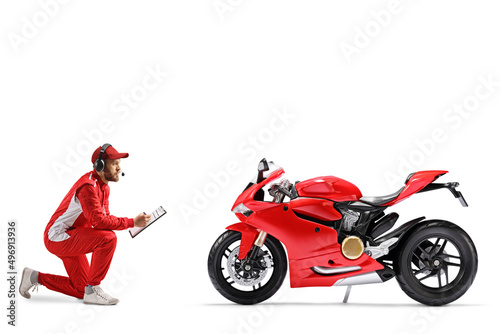 Member of a racing team kneeling in front of a motorbike and writing on a clipboard