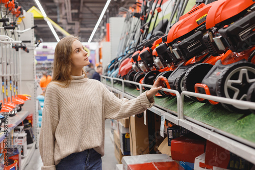 Young woman choosing lawn trimmer in garden equipment store