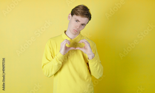 Broken heart guy. Sad guy doing a broken heart with the hands. Isolated on yellow background. Caucasian young guy, 19-20 years old. LOVESICK CONCEPT