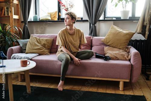 Girl with amputee arm sitting on sofa in the living room with prosthesis, she looking pensive photo