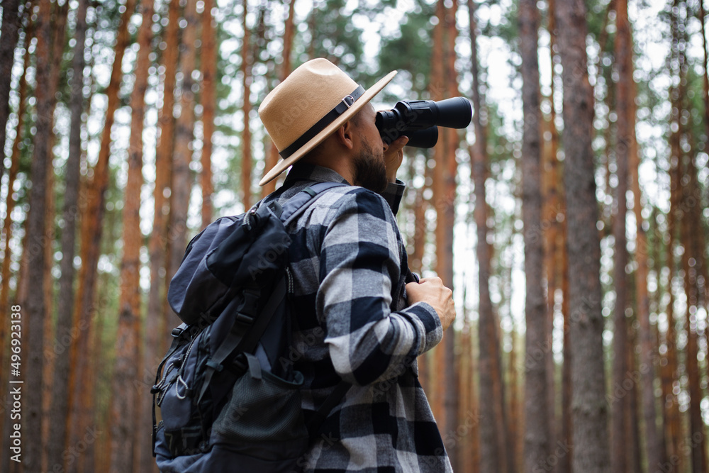 Male tourist looking through binoculars in the forest