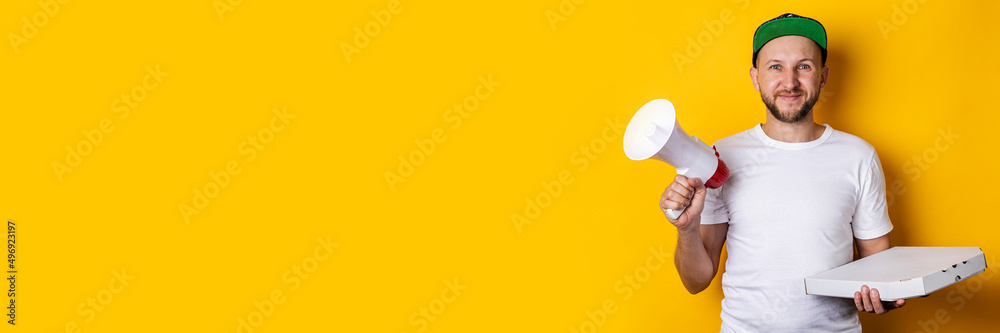 Smiling young man with a megaphone holding packaged pizza on a yellow background. Banner