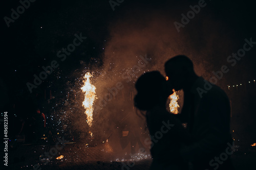 silhouettes of the bride and groom kissing on the background of the fire show