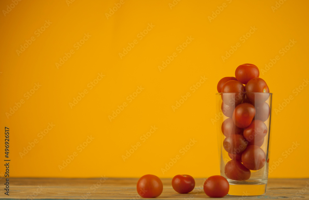 small red cherry tomatoes in a clear glass cup on a wood table background. red vegetables