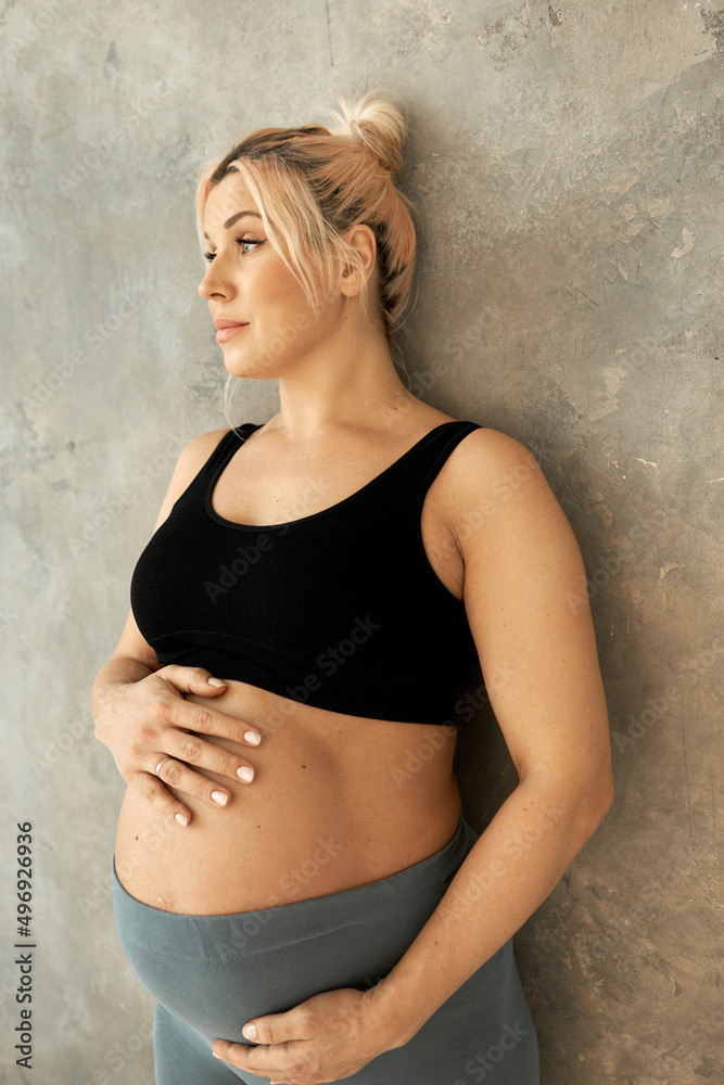 Pregnant woman in third trimester, dressed in comfortable home wear, posing against brown studio wall, looking pensive, standing half turned to camera. Happy pregnancy and motherhood concept Pregnant woman in third trimester, dressed in comfortable home wear, posing against brown studio wall, looking pensive, standing half turned to camera. Happy pregnancy and motherhood concept