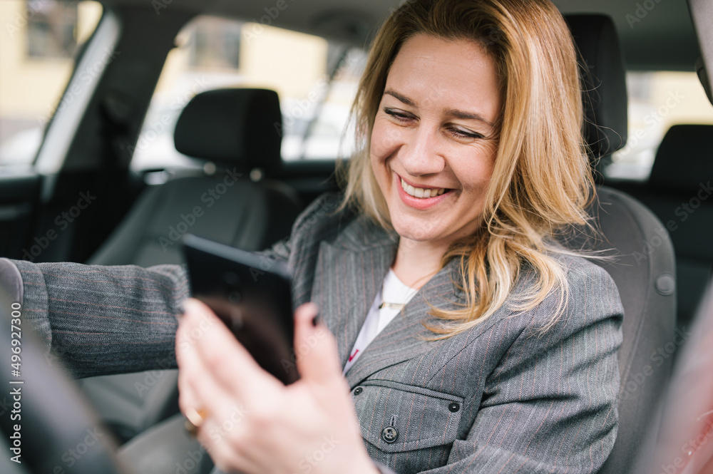 A business woman drives a company car and checks her phone
