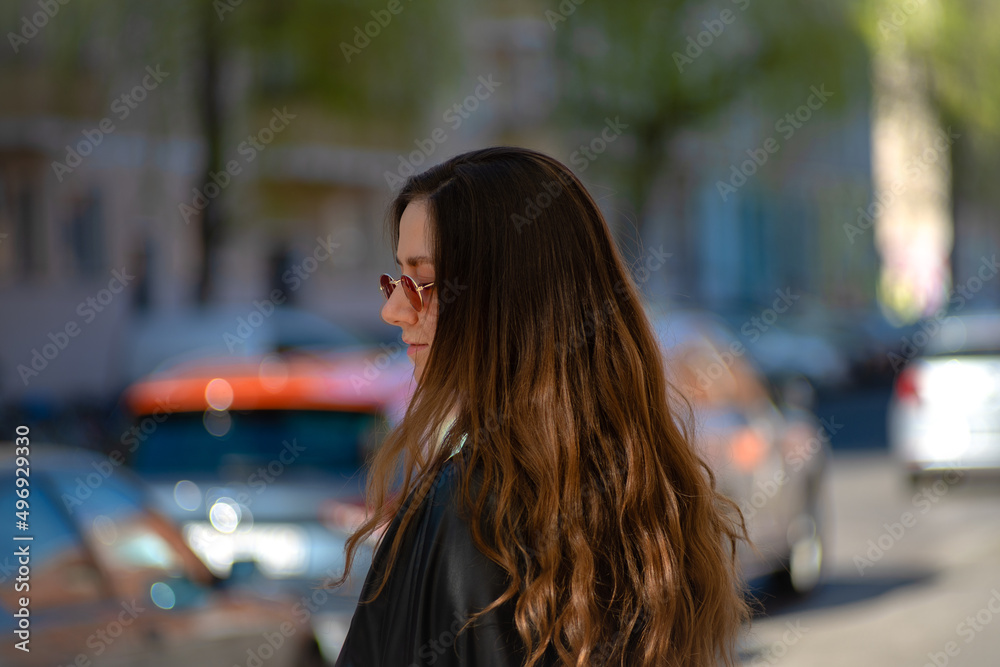 Young brunette woman shaking her hair standing on the side walk waiting to cross the street. Sunny day, spring, sunglasses, fresh