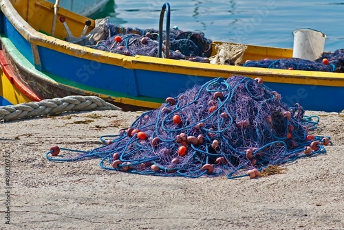 Purple and blue fishing net on the quay in front of a richly colored fishing boat in the Mediterranean Sea,