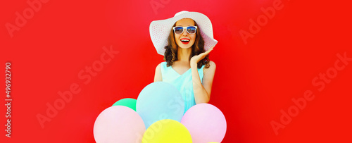 Portrait of happy smiling young woman with colorful balloons wearing summer straw hat on red background, blank copy space for advertising text © rohappy