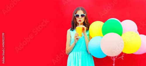 Beautiful young woman drinking juice with colorful balloons on red background, blank copy space for advertising text