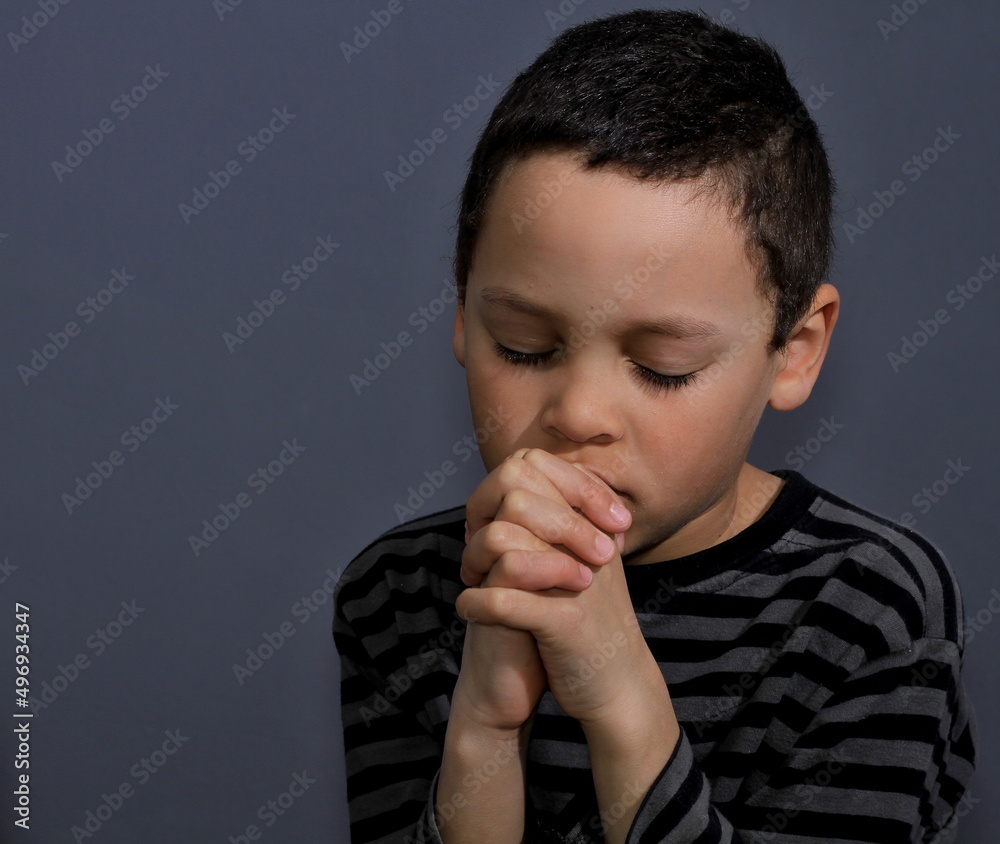 little boy praying to God with eyes closed with grey background stock photo little boy praying to God with eyes closed with grey background stock photo