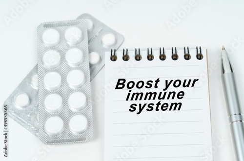 On a white surface are pills in a package, a pen and a notepad with the inscription - Boost your Immune System photo