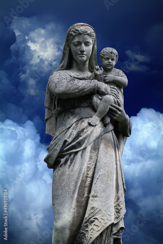 Queen of Heaven. Virgin Mary with baby Jesus Christ. An ancient statue against blue sky background.