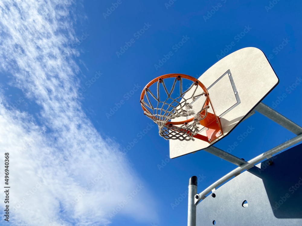 A basketball hoop stands against a clear blue sky with some clouds. Concept of outdoor sport. A basketball hoop stands against a clear blue sky with some clouds. Concept of outdoor sport.