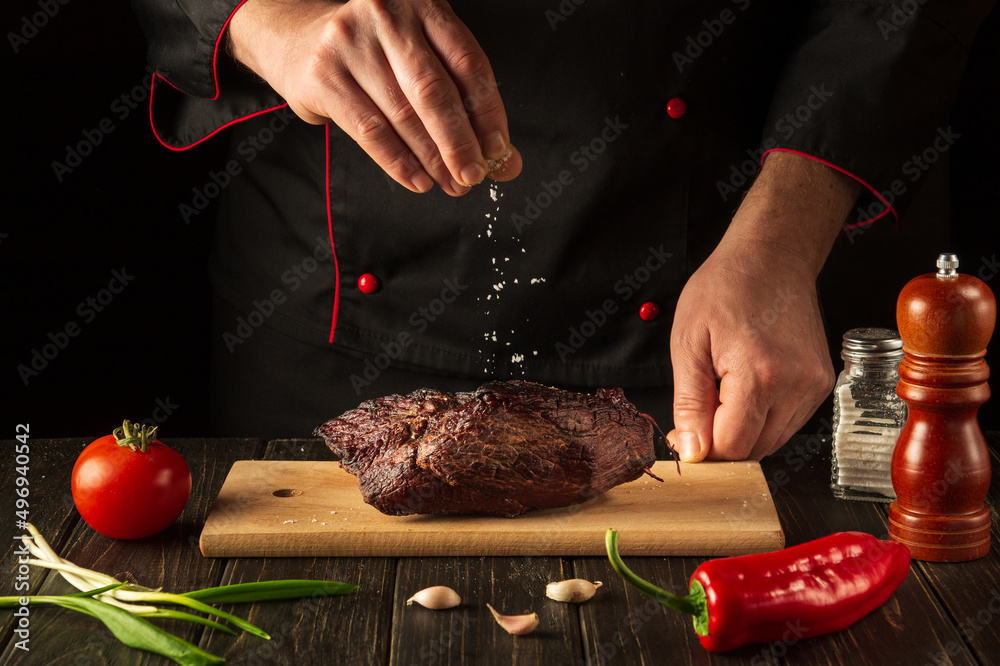 A professional chef sprinkles the baked beef meat with salt. The concept of cooking delicious food. Asian cuisine