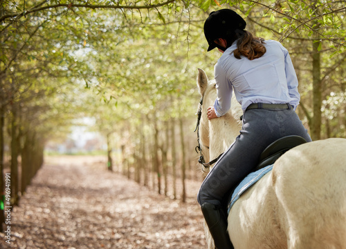 Getting ready to stretch those legs. Shot of an unrecognisable woman horseback riding through the forest during the day.