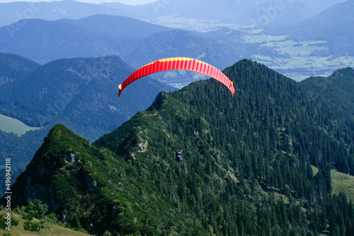 Paraglider tandem shortly after takeoff against wooded mountain ridge