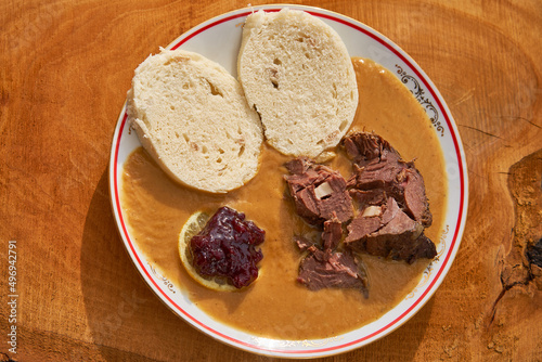 Top view on roasted fallow deer venison in sour cream sauce served with traditional czech bread dumplings, slice of lemon and cranberry marmalade. Traditional hunters seasonal dish from Czech Republic