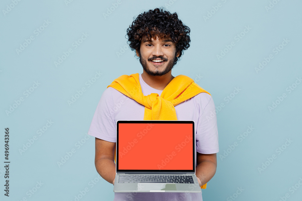 Exultant young bearded Indian man 20s years old wears white t-shirt hold use work on laptop pc computer with blank screen workspace area isolated on plain pastel light blue background studio portrait. Exultant young bearded Indian man 20s years old wears white t-shirt hold use work on laptop pc computer with blank screen workspace area isolated on plain pastel light blue background studio portrait.