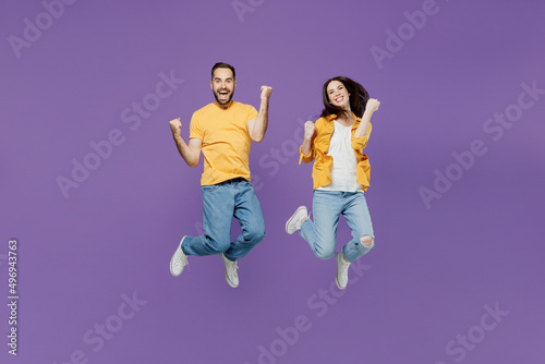 Full body overjoyed excited young couple two friends family man woman together wearn yellow casual clothes jump high do winner gesture clench fist isolated on plain violet background studio portrait.