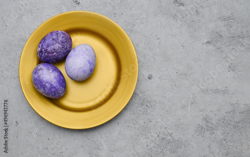 Easter eggs in a very peri color lie on a golden plate on a marble gray background. A postcard with a place for the text.