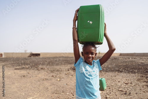 Fototapeta Arid African countryside with a young child lifting a heavy water canister on he