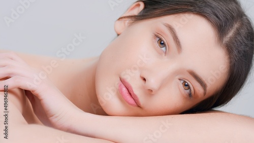 Close-up beauty portrait of young dark-haired woman with perfect skin lays her head on her arms and looks at camera | skincare products advertising concept.