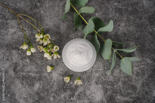   White face cream on dark, granite background with white flowers and eucalyptus leaves.  