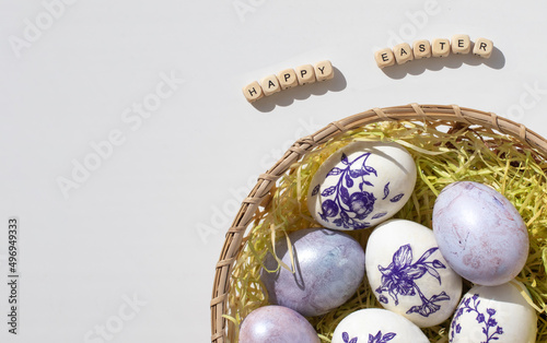 Easter concept. Purple eggs in a wicker basket with straw on a white background. Minimalism. 