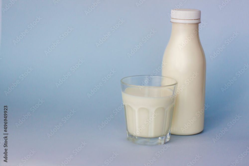 A glass and a bottle of white milk, highlighted on a blue background, close-up. A glass and a bottle of white milk, highlighted on a blue background, close-up.