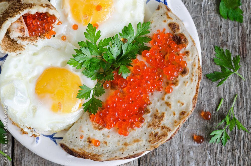 Fried eggs with pancakes and red caviar, close-up, on an old wooden background. View from above Fried eggs with pancakes and red caviar, close-up, on an old wooden background. View from above