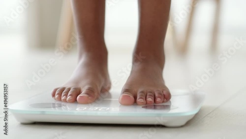 Legs of black girl standing on scale to measure weight. African American Female bare feet with weight scale at home. dieting, control and measuring  photo