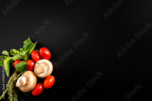 Mushroom, cherry tomato and herbs on black background