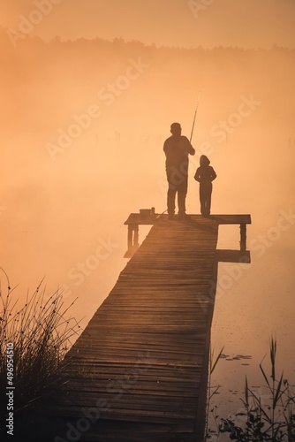 Beautiful morning scene by the lake. Father and son fishing in the light of the rising sun.