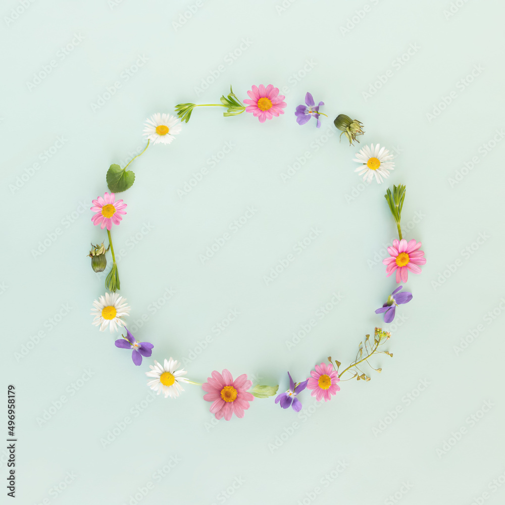 Creative decorative round frame or border made of spring or summer flowers on isolated pastel green background with copy space. Minimal flat lay. Gift or greeting card. Nature blooming concept.