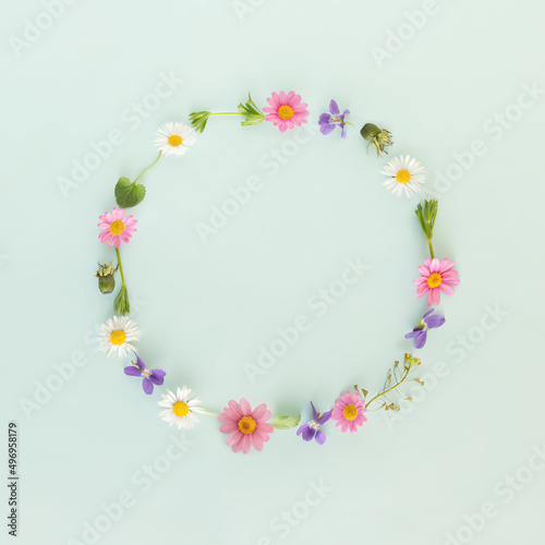 Creative decorative round frame or border made of spring or summer flowers on isolated pastel green background with copy space. Minimal flat lay. Gift or greeting card. Nature blooming concept.
