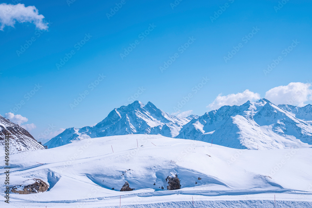 Tracks on snow covered landscape slope against blue sky