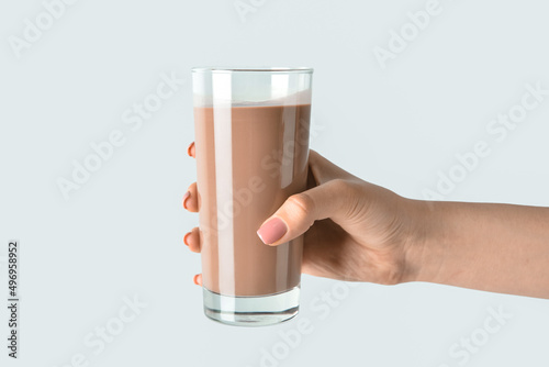 Female hand holding glass of delicious chocolate milk on grey background photo