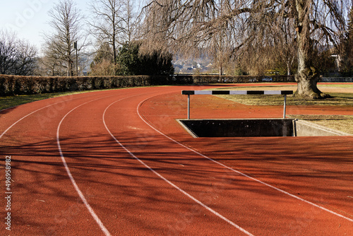 sportanlage munot schaffhausen switzerland: big red round track with water hurdle, weeping willow in the right edge of the picture, sport is healthy for young and old, without people, autumn day