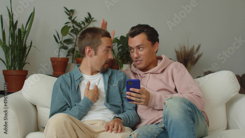 Lgbt men are sitting on the sofa in the living room and discussing how to design their flat and quarrel a little