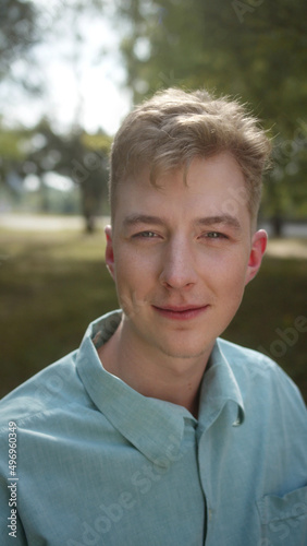 A young handsome man in a blue shirt is staring at the camera, blinking his eyes and contemplating 