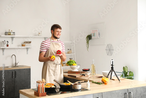 Young man with bell peppers recording cooking video tutorial in kitchen